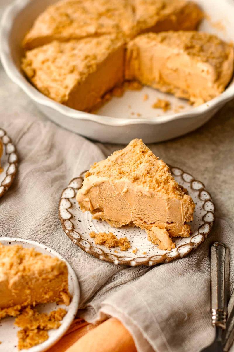 Slice of pumpkin ice cream pie on a plate in front of the rest of the pie still in a pie dish.