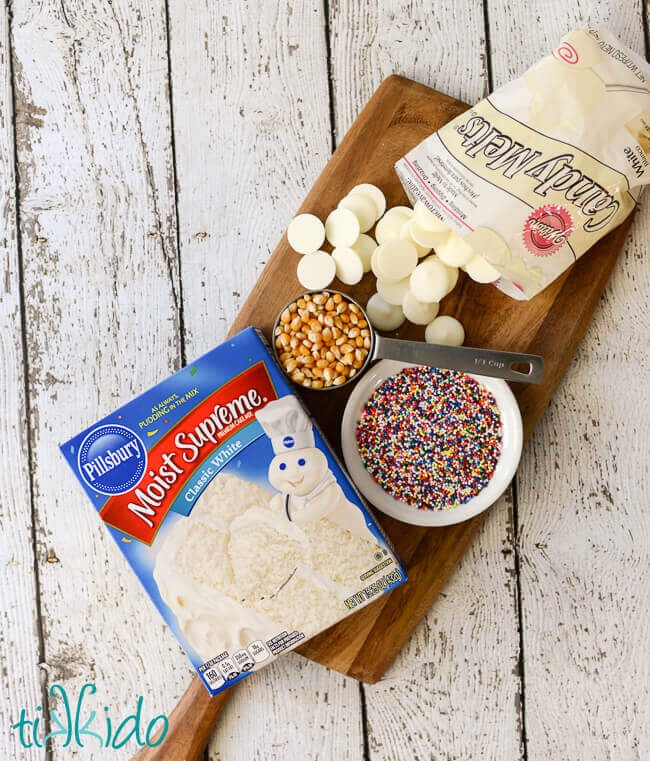 Ingredients for birthday cake popcorn recipe on a wooden cutting board.