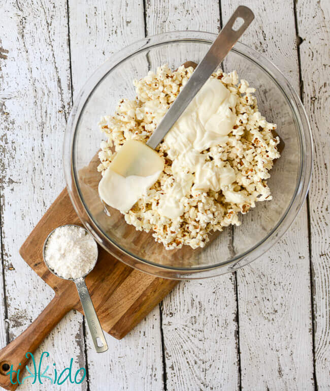 Melted white chocolate being stirred into popcorn to make birthday cake popcorn.