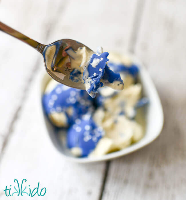 Cracked Blue Magic Shell Ice Cream Topping and vanilla ice cream on a spoon, with the bowl of ice cream in the background.