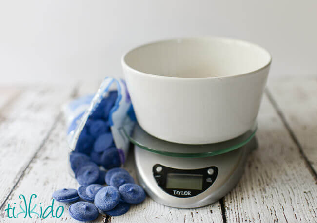 Blue chocolate melts being weighted in a white bowl on a kitchen scale to make Blue Magic Shell Ice Cream Topping.