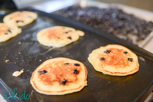 Buttermilk pancakes with fresh blueberries on a griddle.