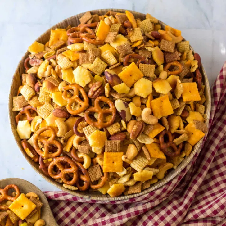 Chex mix made in a slow cooker, in a bowl, next to red and tan gingham cloth.