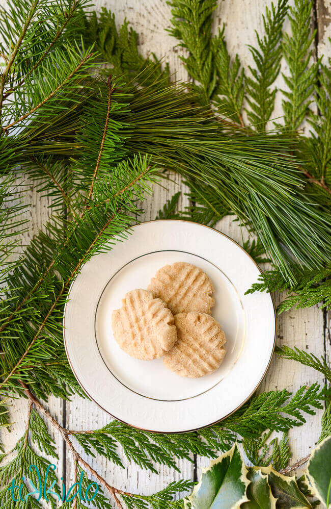 three browned butter cookies on a white plate, surrounded by fresh evergreen branches.