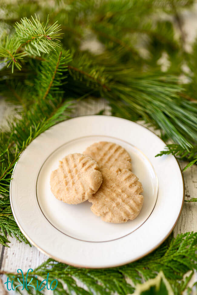 three browned butter cookies on a white plate, surrounded by fresh evergreen branches.