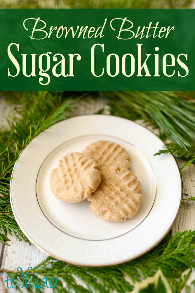 browned butter sugar cookies on a white plate, surrounded by fresh evergreen branches.