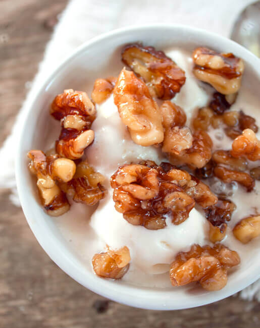 Wet walnuts ice cream topping over vanilla ice cream in a white bowl.
