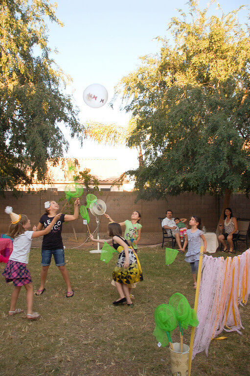Children playing badminton with butterfly nets and a clear balloon with paper butterfly shapes inside.