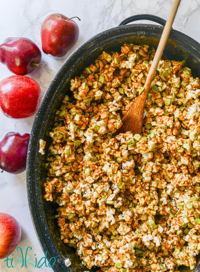 Popcorn and apple pieces in a roasting pan and covered with caramel to make Caramel Apple Popcorn