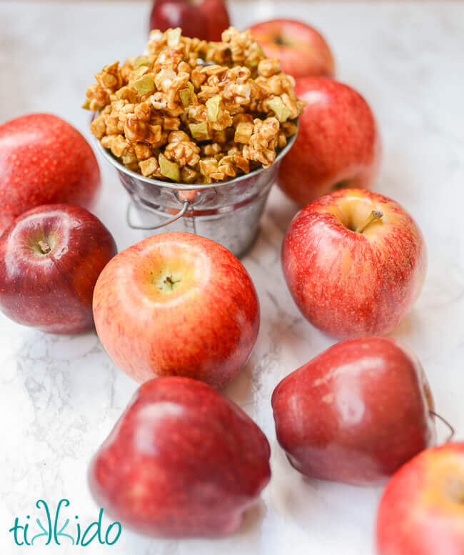 Caramel Apple Popcorn in a metal pail surrounded by apples.