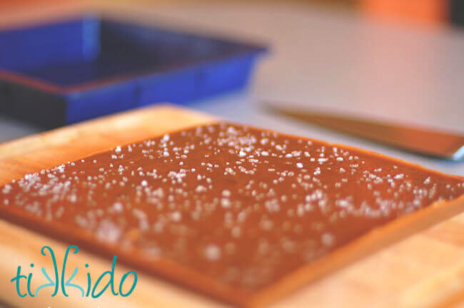 Homemade salted caramels turned out on a wooden cutting board, square  blue silicone pan behind