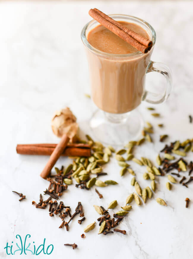 Homemade chai in a clear mug surrounded by whole spices.