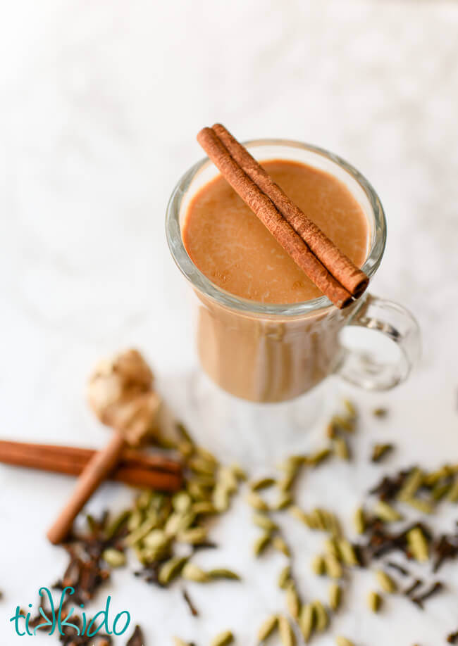 Homemade chai in a clear mug surrounded by whole spices.