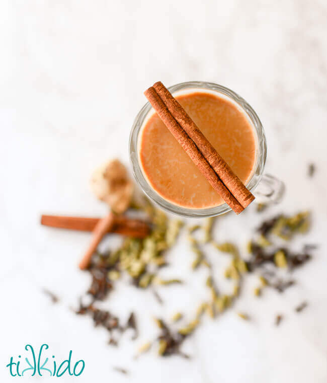 Homemade chai in a clear mug surrounded by whole spices.