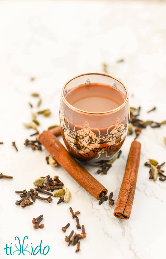 Homemade chai in a clear mug surrounded by whole spices.