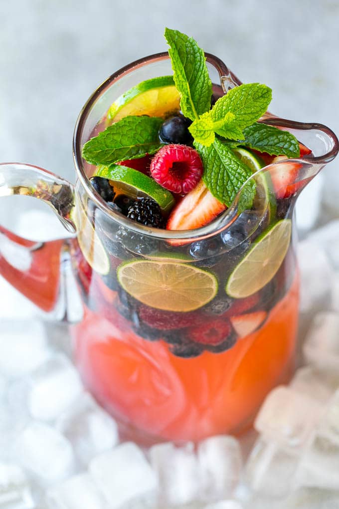 Pitcher of pink Berry Champagne Punch, filled with fresh berries and slices of lime, and garnished with a sprig of fresh mint.