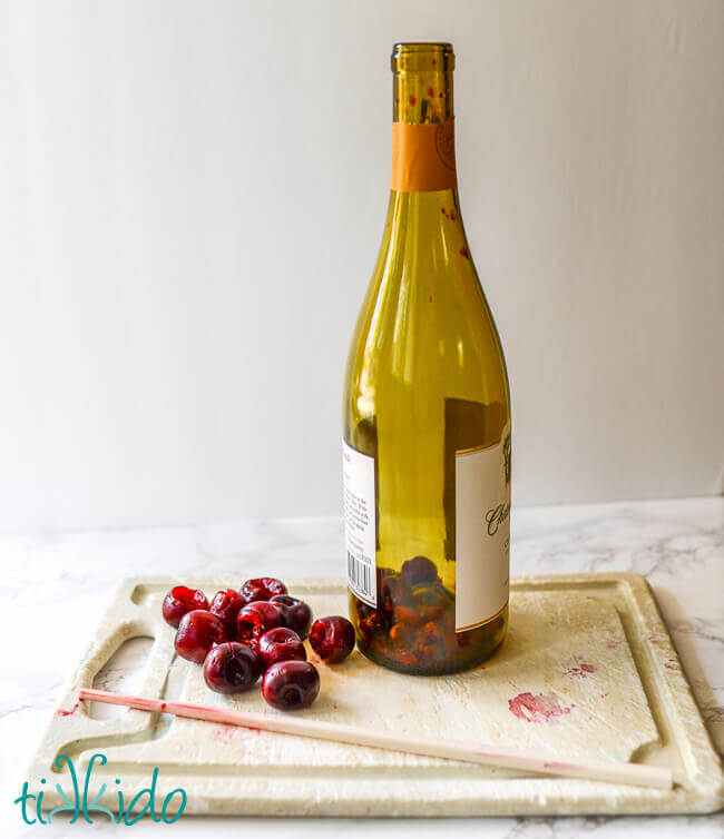 Cherries being pitted using a chopstick and and empty wine bottle.
