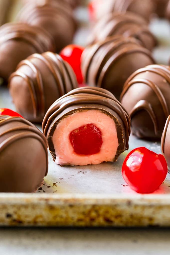 Closeup photo of chocolate covered cherries, next to maraschino cherries and with one chocolate covered cherry candy sliced open.