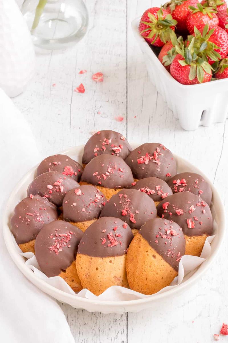 Chocolate covered strawberry madeline cookies a white bowl on a white wooden surface.