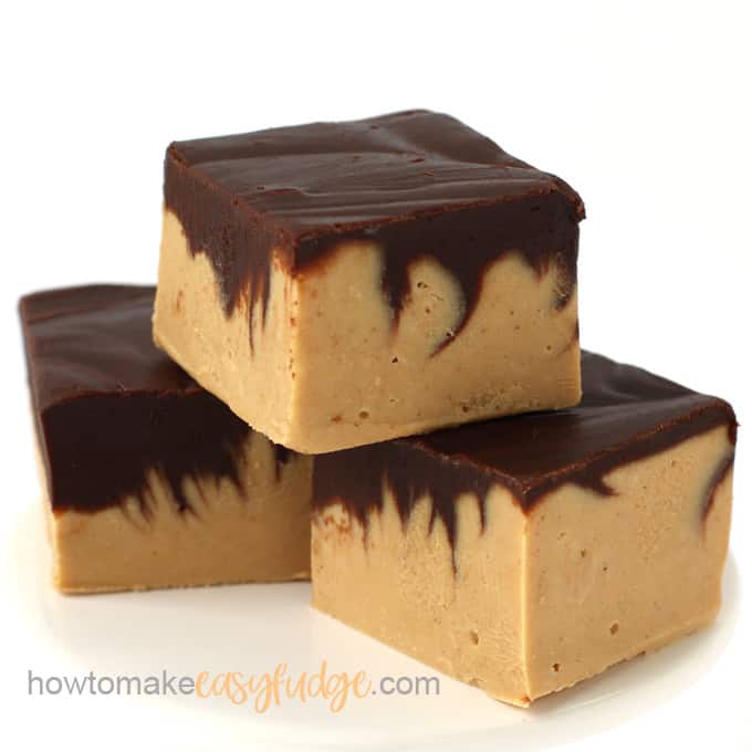 Three pieces of chocolate peanut butter fudge stacked on a white surface.