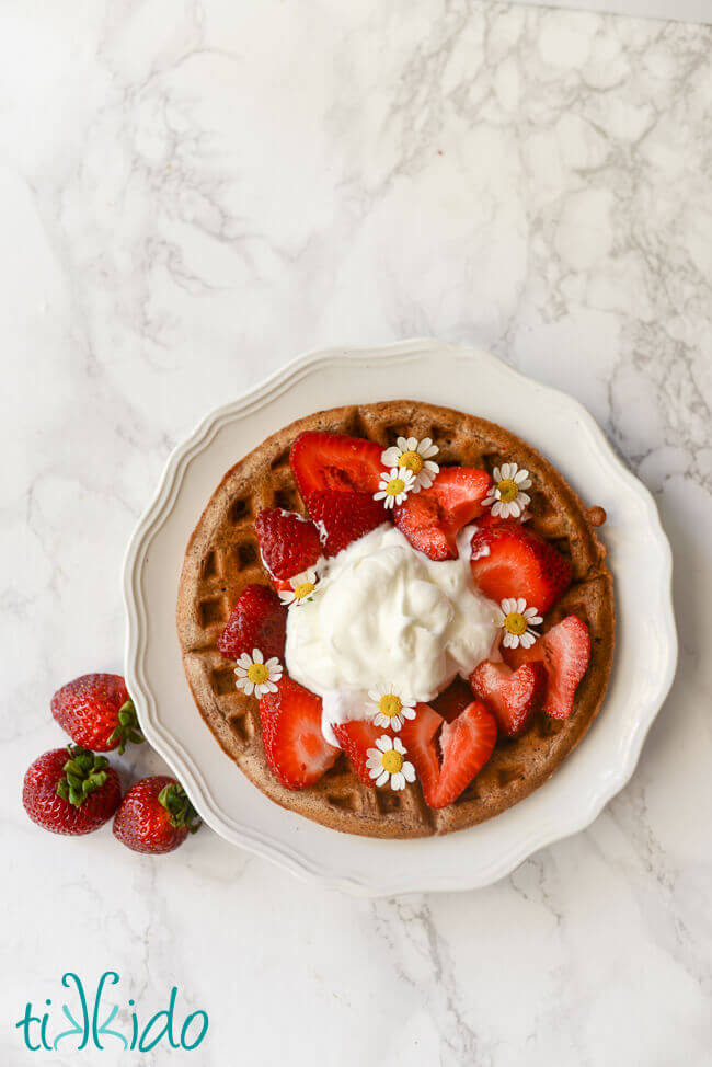 Chocolate waffle topped with strawberries and whipped cream on a white marble background.