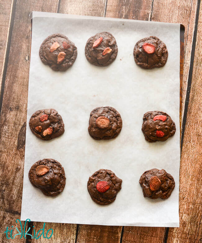 Freshly baked Chocolate Covered Strawberry Cookies on parchment paper on a wooden table.