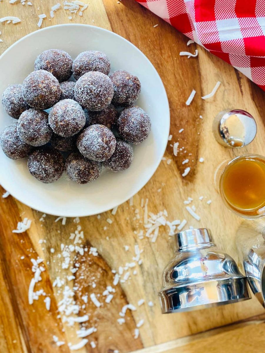 Coconut rum balls in a white dish on a wooden cutting board.