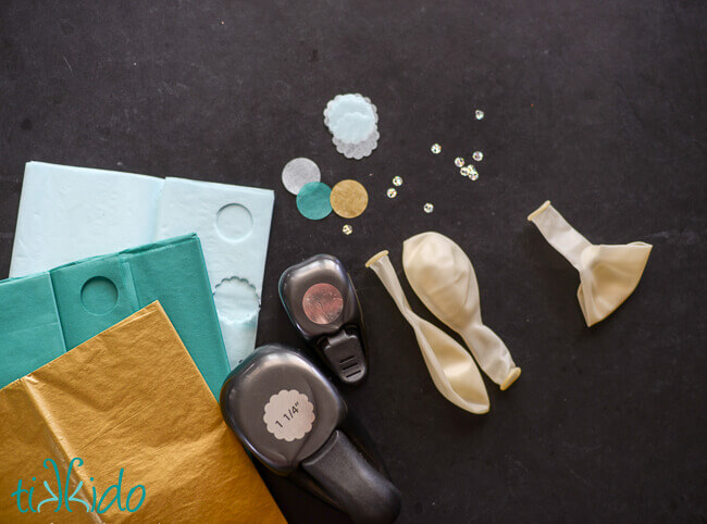 Clear balloons, sequins, tissue paper, and paper punches on a black background.