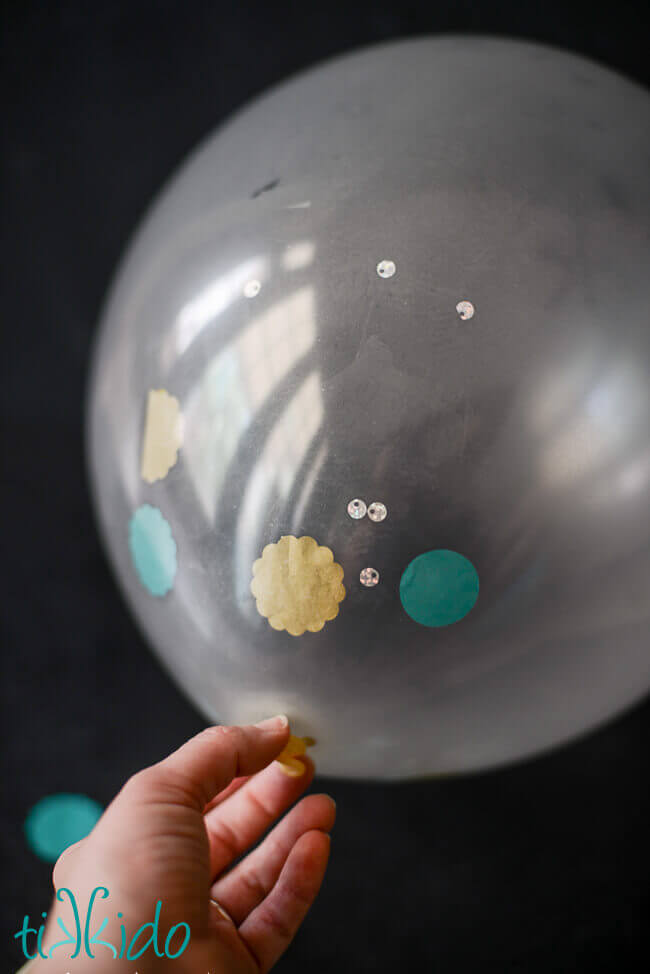 Clear balloon filled with tissue paper confetti and sequins, on a black background.