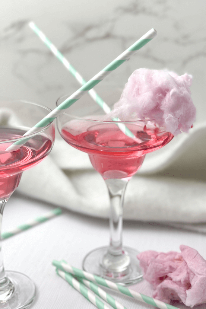 Two margarita glasses filled with cotton candy margarita, garnished with a tuft of pink cotton candy.