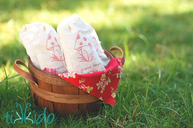 Wooden apple basket filled with three muslin favor bags full of salted caramels, sitting in dewy grass