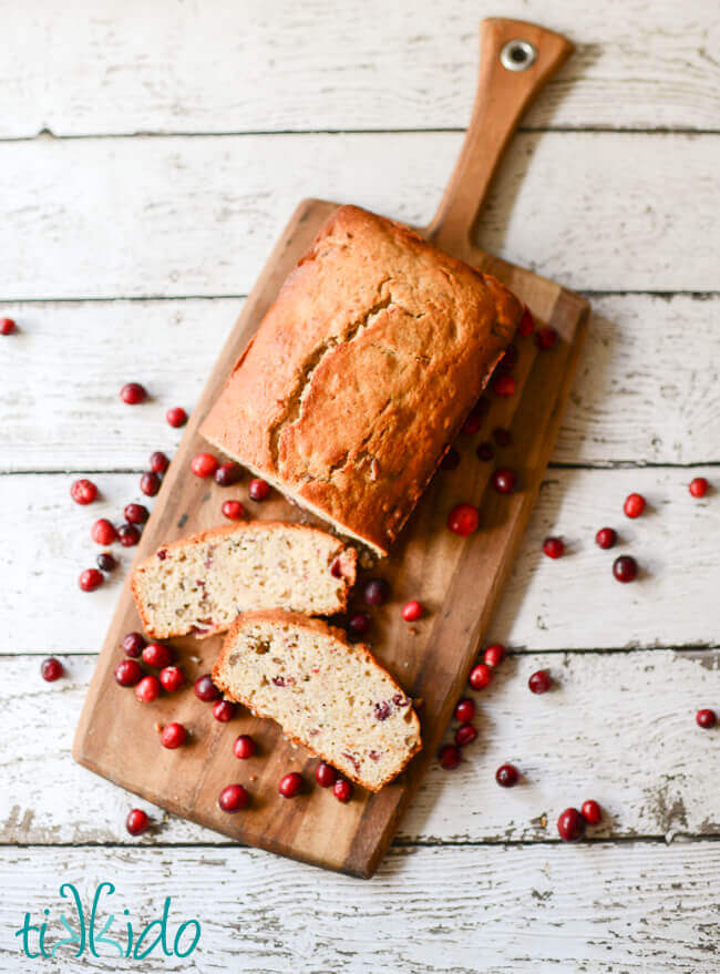 Sliced Cranberry Nut Bread on a cutting board surrounded by cranberries.