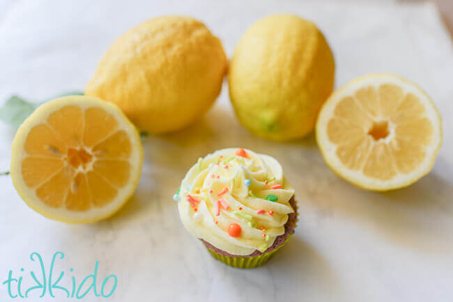 Cupcake topped with lemon buttercream frosting and sprinkles, surrounded by lemons.