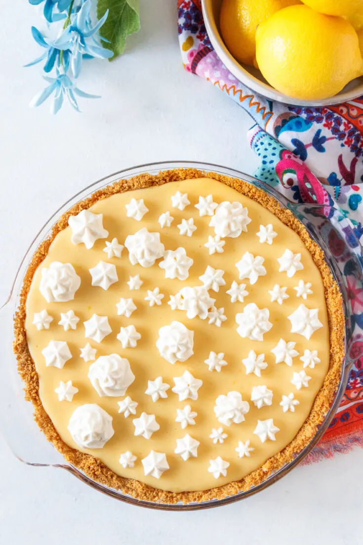 Creamy lemon pie with graham cracker crust in a pie dish, next to a floral tea towel.