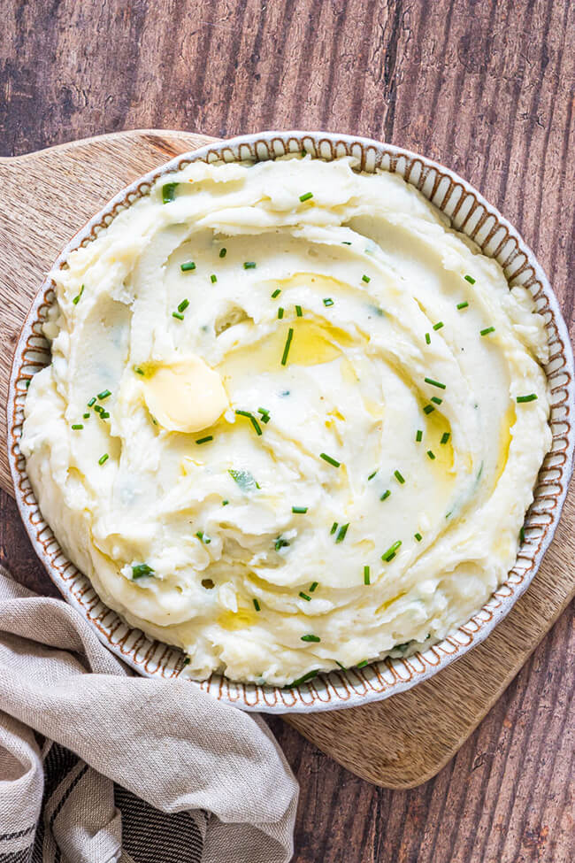 bowl of crockpot mashed potatoes with butter and chives on a wooden table.