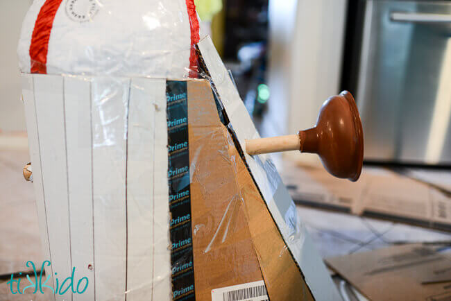 Store bought baseball pinata being taped and glued to cardboard to form a Dalek Piñata