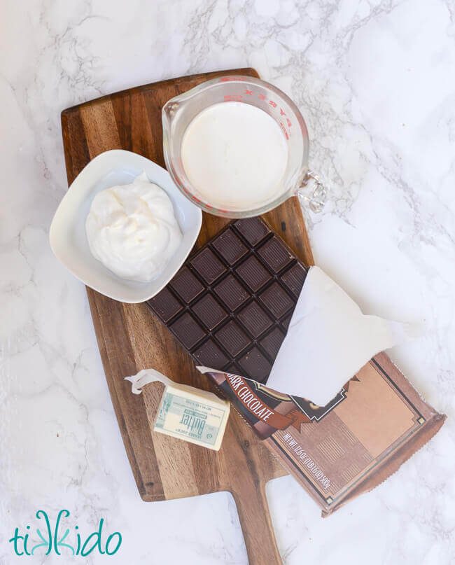 Ingredients for Dark Chocolate truffles, cream, sugar, butter, dark chocolate, on a wooden cutting board