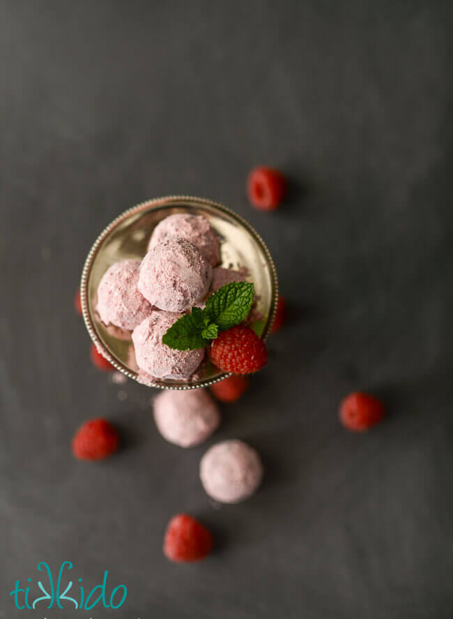 Raspberry dark chocolate truffles dusted with raspberry powdered sugar, surrounded by fresh raspberries.