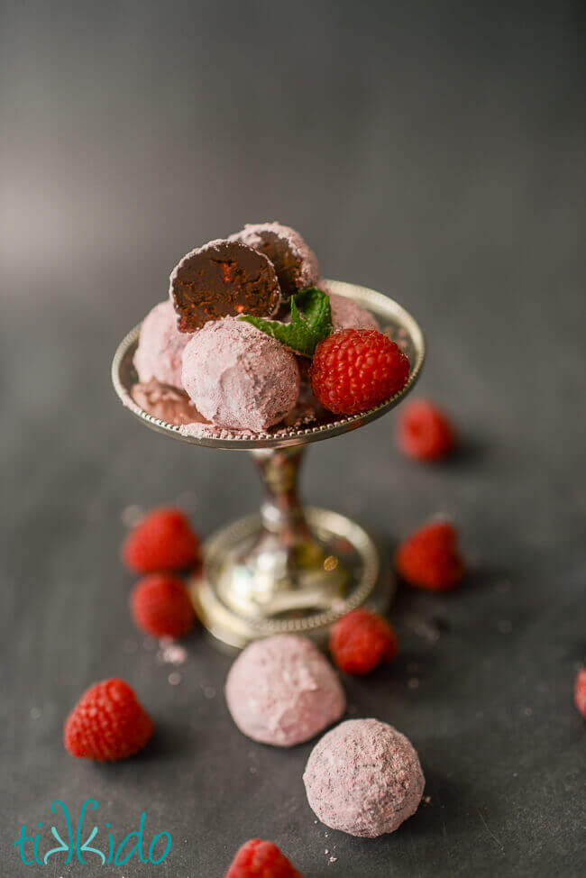 Chocolate raspberry truffles cut in half, dusted with raspberry powdered sugar, surrounded by fresh raspberries.