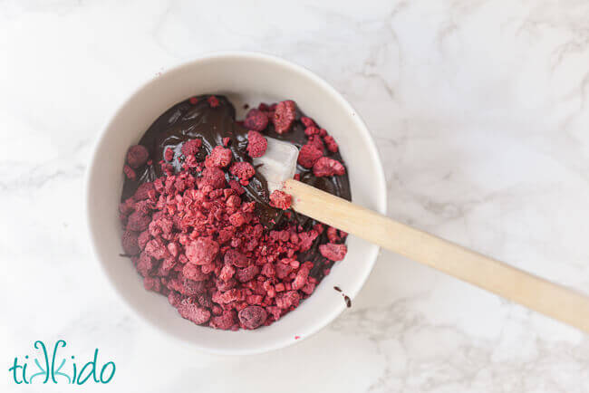 White bowl of dark chocolate ganache being mixed with freeze dried raspberries to make chocolate raspberry truffles.