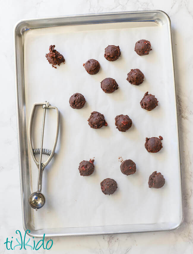 Chocolate raspberry truffles scooped out on a parchment lined baking tray, silver scoop sitting on the tray.