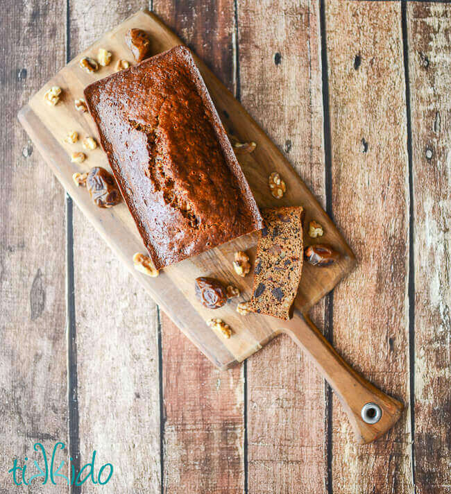Loaf of date nut quick bread sliced on a wooden cutting board.