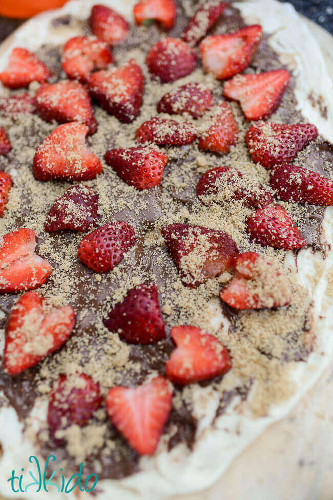 Uncooked dessert pizza with nutella, strawberries, and brown sugar, on a wooden pizza peel