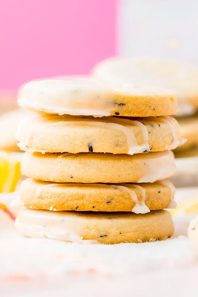 Stack of earl grey shortbread cookies with lemon glaze in front of a pink background.