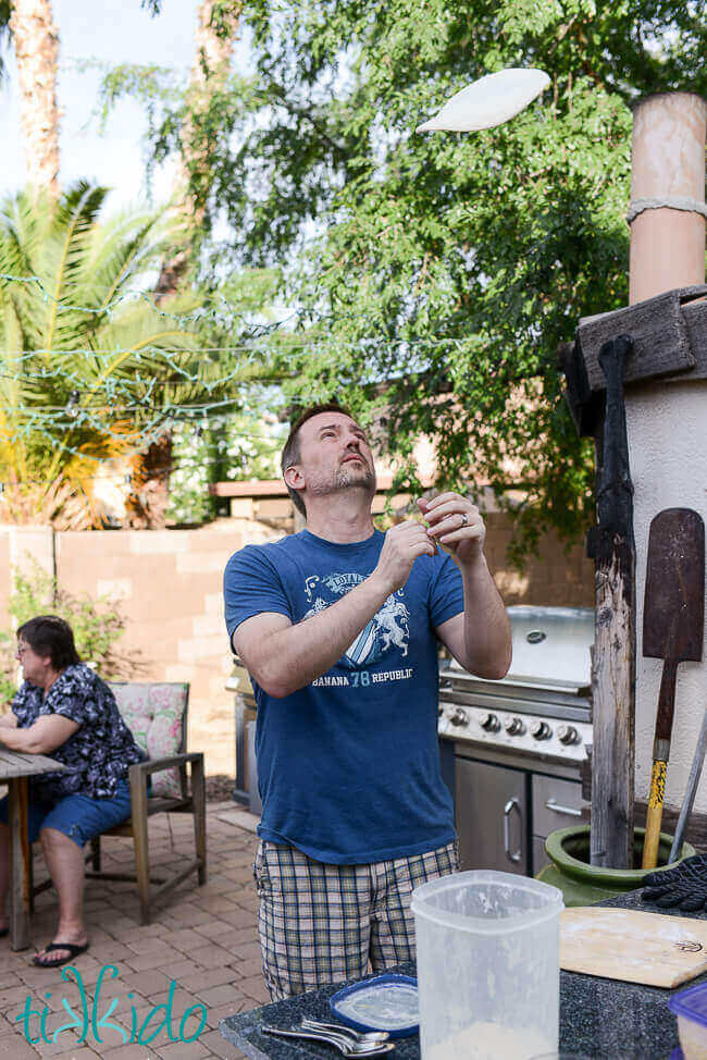 Man tossing pizza dough in front of a wood fired pizza oven.