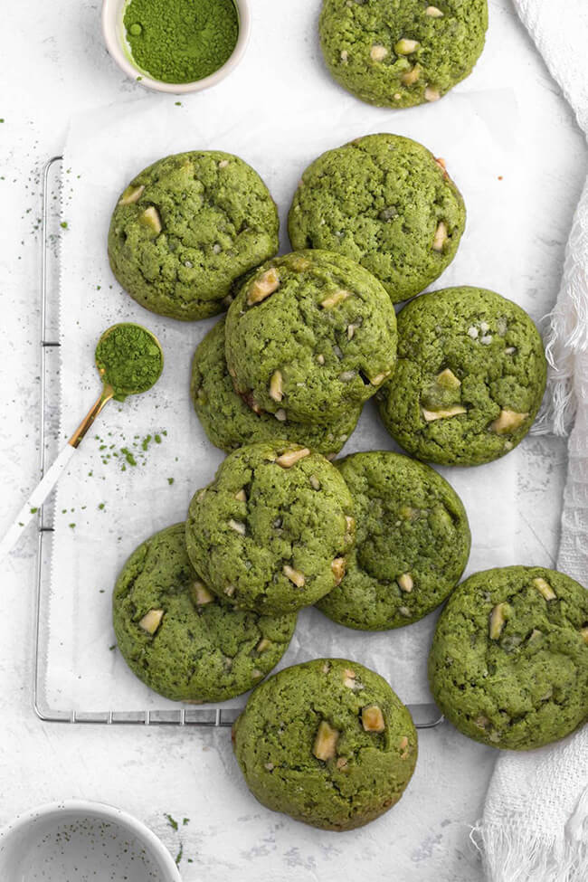 Soft, Chewy, Vegan matcha green tea cookies on parchment paper, next to a spoon of matcha powder.