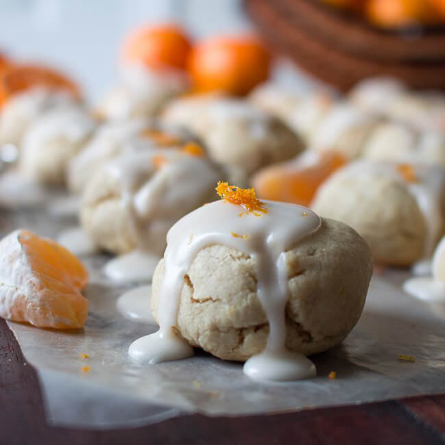 Chewy mandarin orange cookies topped with orange glaze and orange zest, on parchment paper.