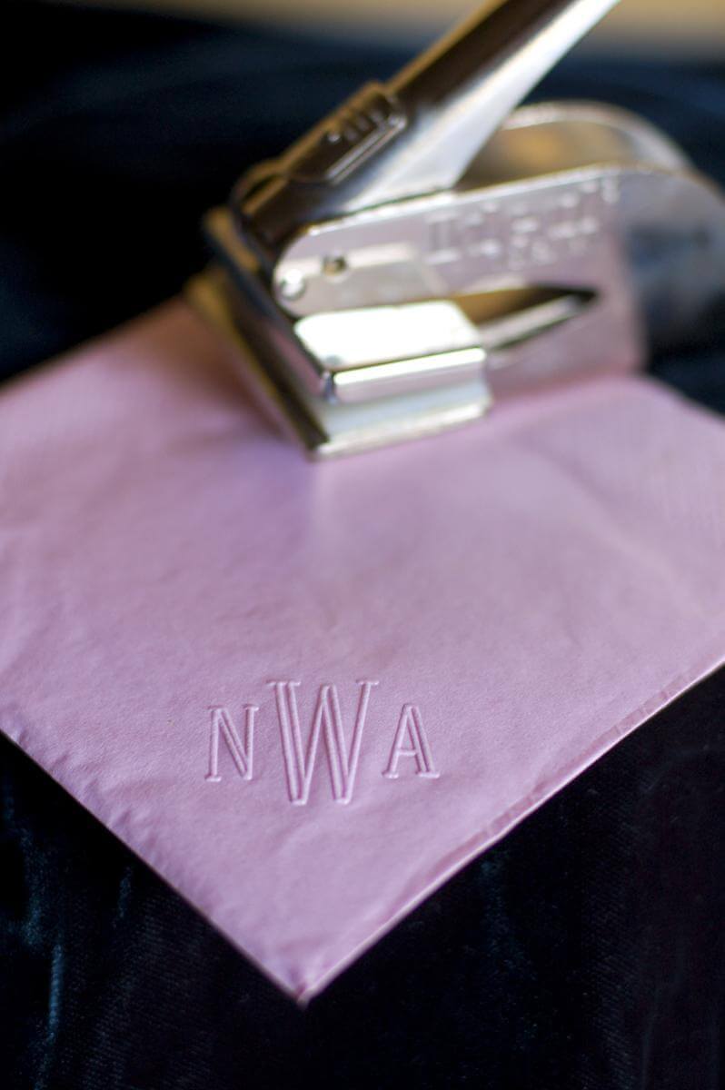 Purple paper napkin with an embossed monogram, monogram embosser in the background.