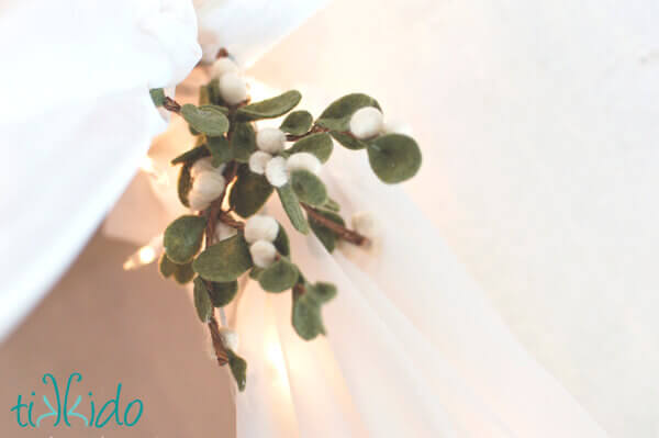 Felt mistletoe made with felt ball berries hanging from white curtains.
