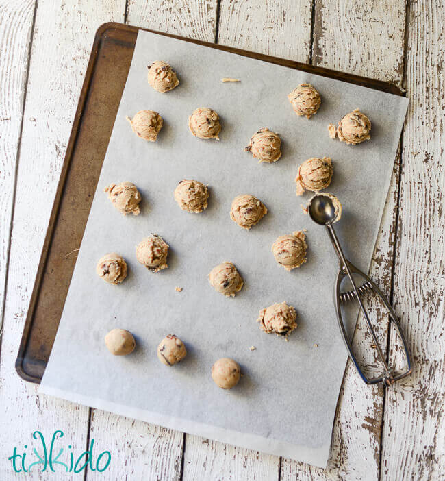 Dough for Figgy Pudding Cookies being scooped out on parchment paper lined cookie sheet.